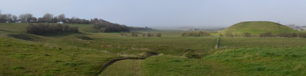The Motte and Bailey, a wide view of a grass hill on which the castle would have stood with circular dry ditch surrounding it.