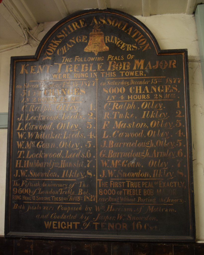 Old wooden notice board painted with the title "Yorkshire Association Change Ringers". Notice Says The following peals of Kent Treble Bob Major were rung in this tower 1877. The names of the ringers are listed and weights of the tenor bell