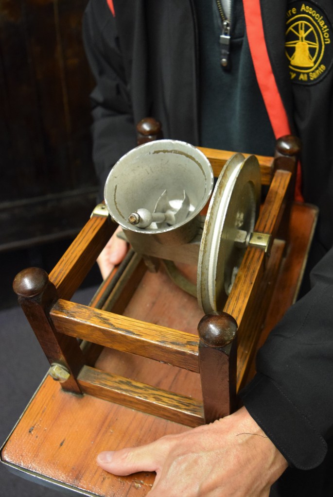 Photo of a handheld model of church bell secured in a wooden frame
