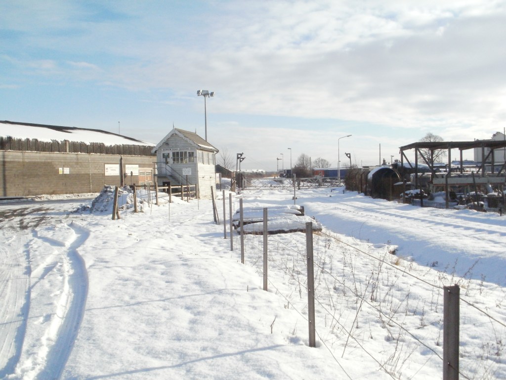 Snow covered rail tracks at gated level crossing with signal box