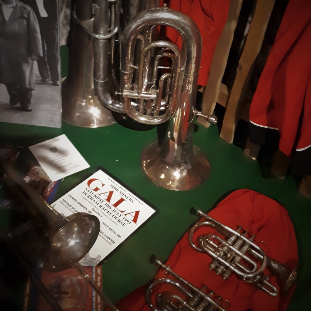 A selection of brass band instruments, band uniform and a miners band concert programme