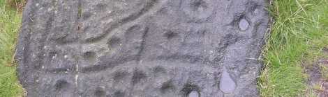 A large stone embedded in moorland, with strange ancient circular depressions and criss-cross grooved marks