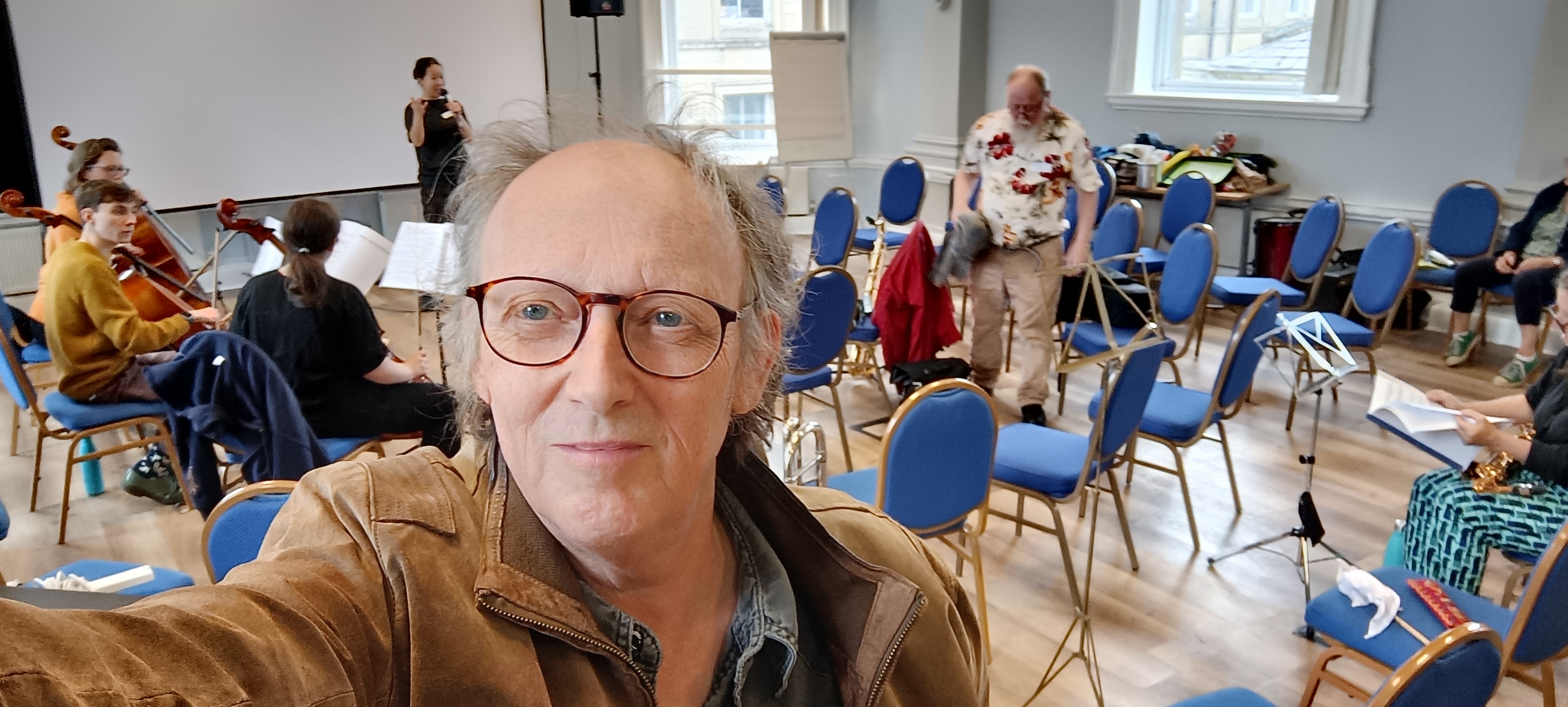 Author in the foreground with musician arriving, the narrator in background with microphone rehearsing her lines