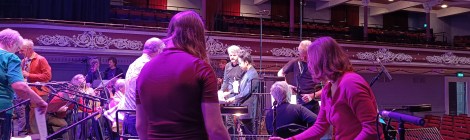 Musicians are setting up, the narrator and conductor are discussing the final arrangement before the performance in the ornate theatre hall