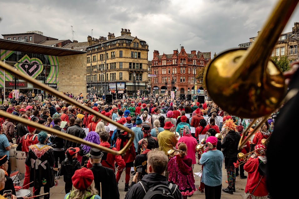 Mass street bands at the First Honk UK in Bradford 2025 seen from behind the trombones on the steps of town hall looking Centenary Square.